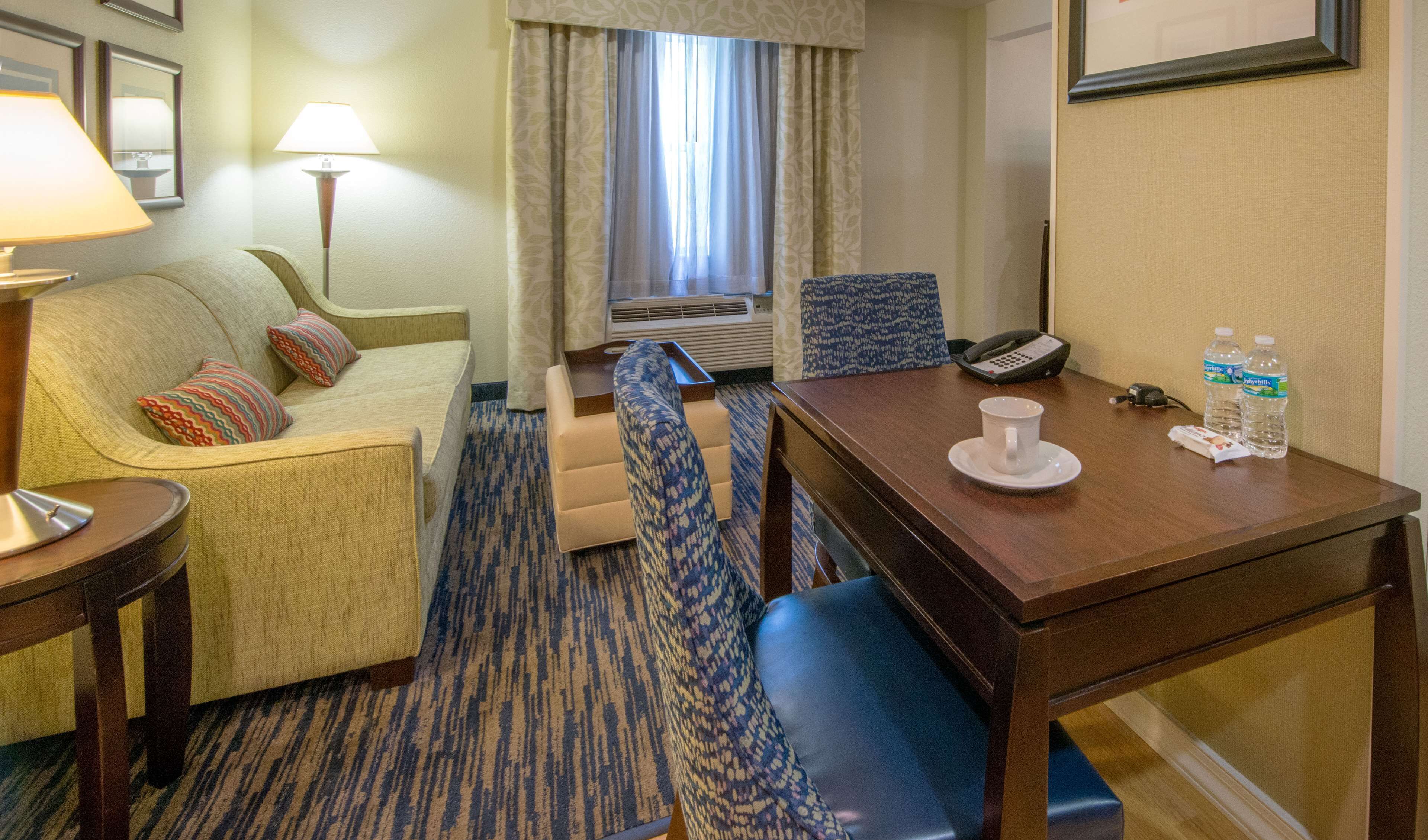Habitación de hotel con sofá, sillón y una pequeña mesa de comedor con una taza y botellas de agua.