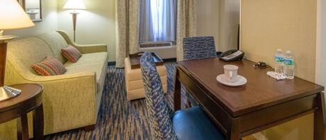 Habitación de hotel con sofá, sillón y una pequeña mesa de comedor con una taza y botellas de agua.