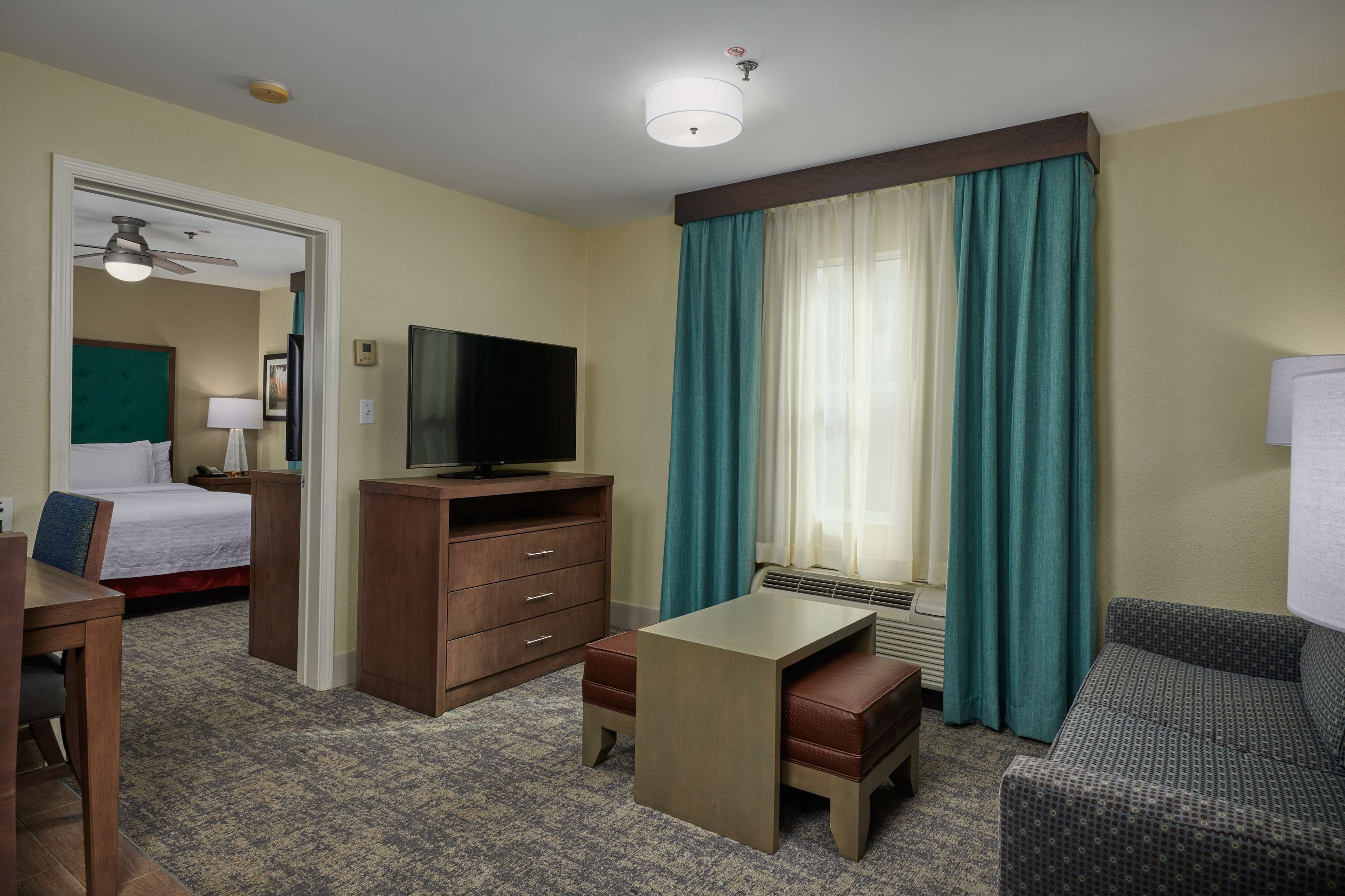 Une chambre d’hôtel comprenant un lit, un bureau, une télévision, une commode et une fenêtre avec des rideaux.