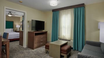 Une chambre d’hôtel comprenant un lit, un bureau, une télévision, une commode et une fenêtre avec des rideaux.