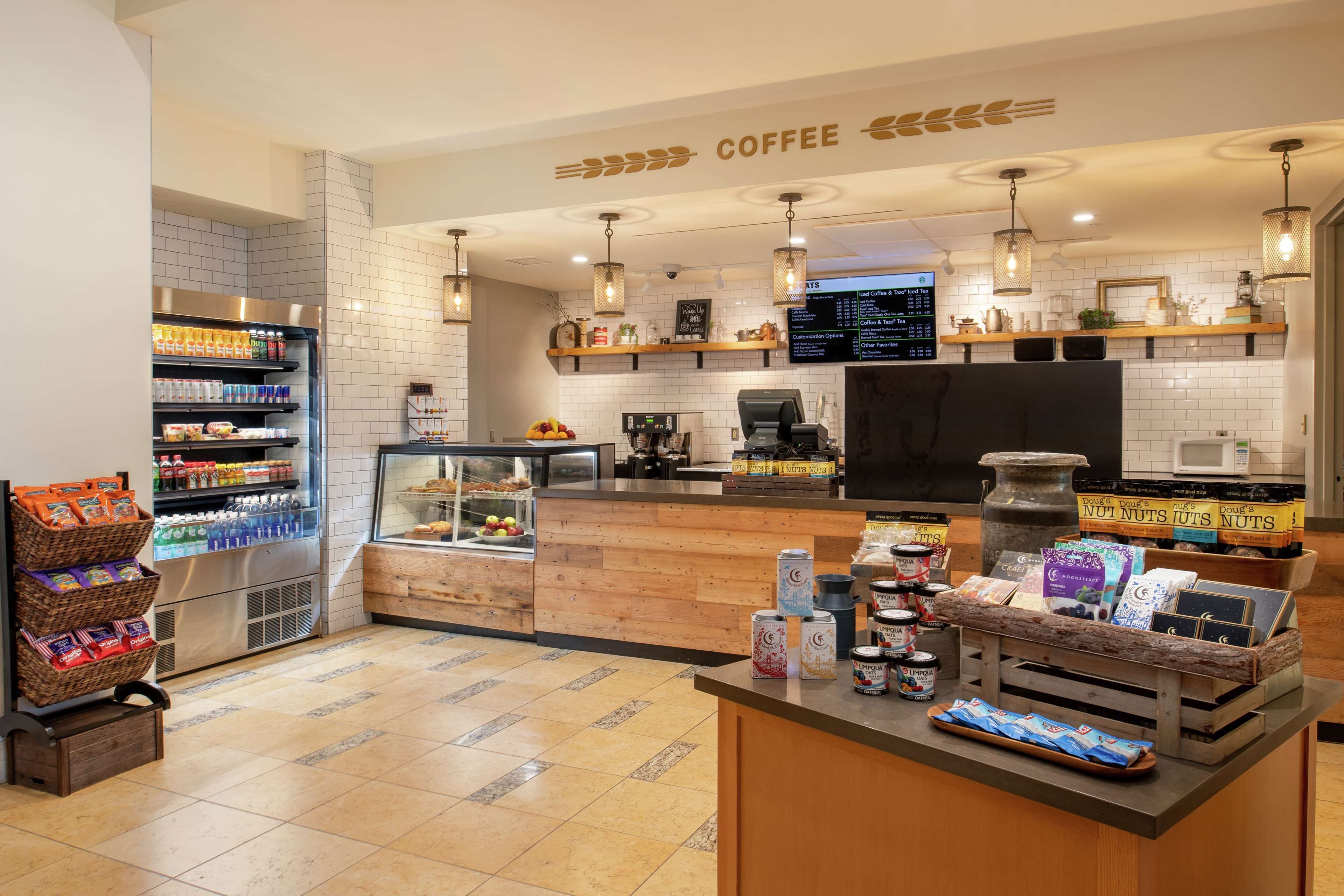A coffee shop interior with a counter, shelves with snacks, a coffee machine, and a menu display.