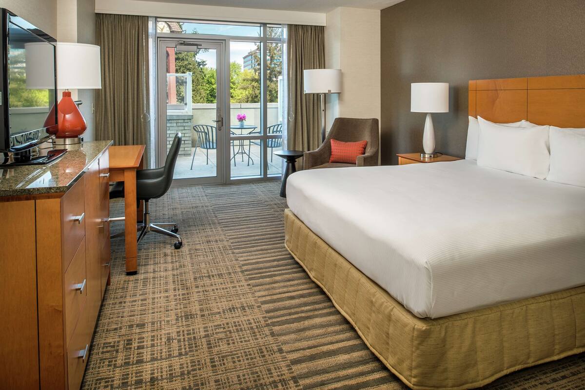 A hotel room with a large bed, a desk with a chair, a TV, and a balcony with a table and chairs.
