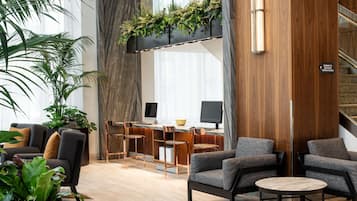 A modern hotel lobby with a seating area, a desk with computers, and a staircase.
