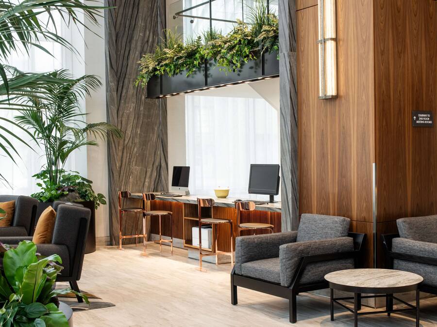 A modern hotel lobby with a seating area, a desk with computers, and a staircase.