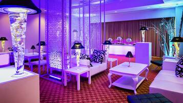 Relax in a stylish room with a plush sofa, armchairs, and a floor lamp, surrounded by elegant decor and a reception desk nearby.