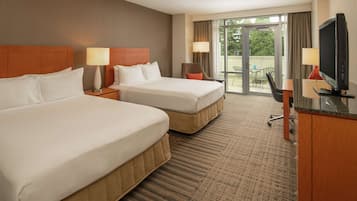 A hotel room with two beds, a desk with a TV, and a balcony with a view.
