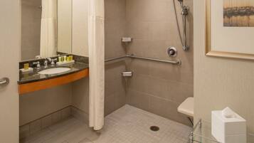 A bathroom with a shower, a sink with toiletries, a glass shelf, and a framed picture on the wall.