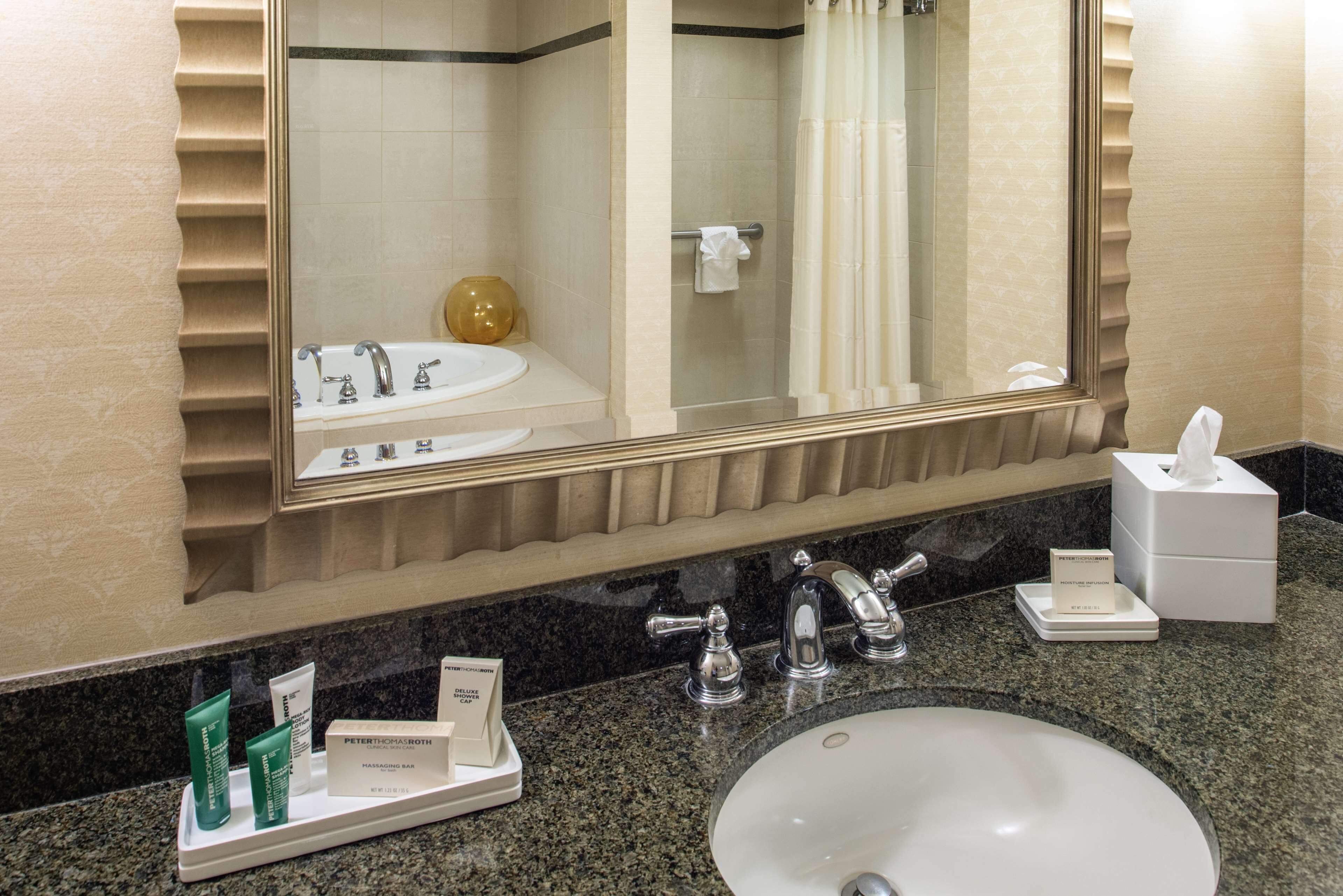 A hotel bathroom with a large mirror, a sink, and toiletries on a tray.