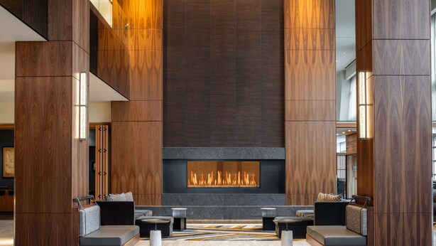 A modern lobby with a central fireplace, seating areas, and wooden paneling. - Hilton Vancouver Washington (Vancouver)