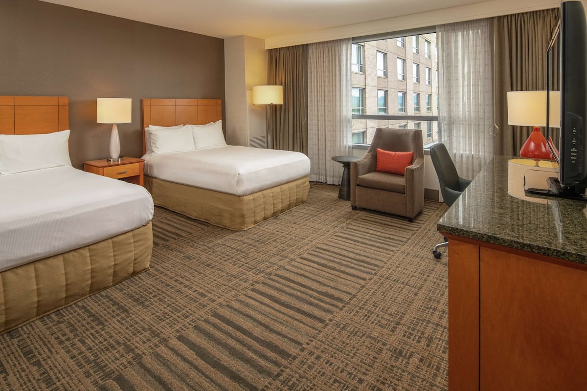 A hotel room with two beds, a desk, a chair, and a TV.