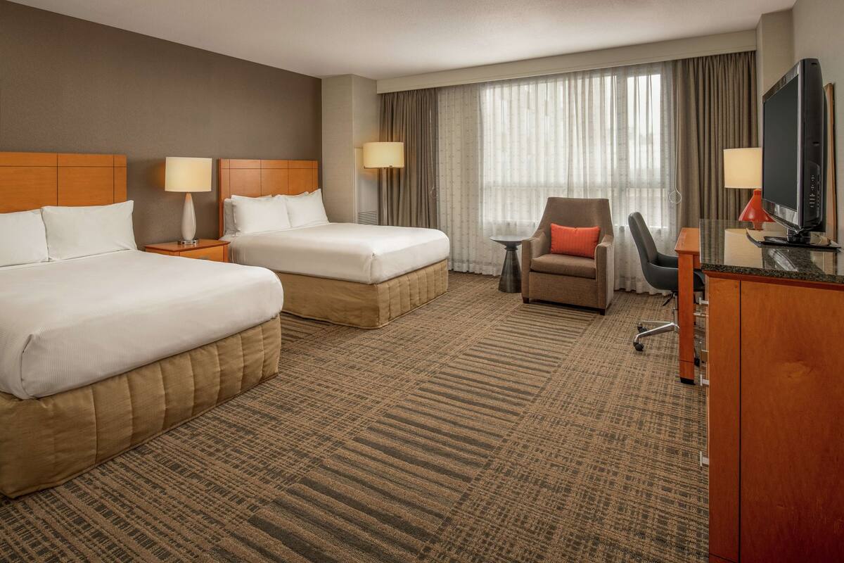 A hotel room with two beds, a desk with a TV, a chair, and a small table.