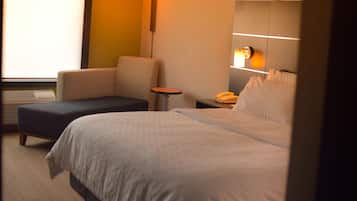Habitació d'hotel amb un llit, una cadira, una taula petita i una làmpada de nit.