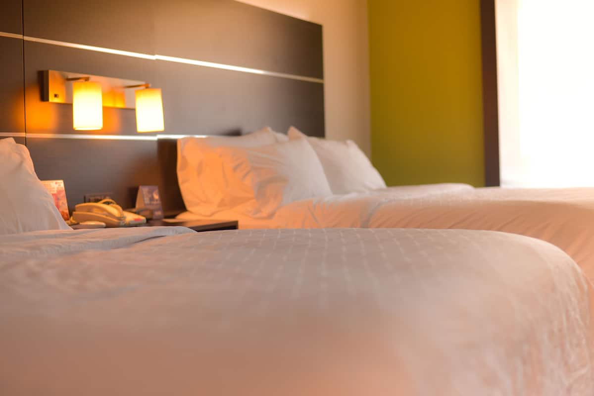 Et hotelværelse med en stor seng, et natbord med en lampe, og en vægmonteret lampe.