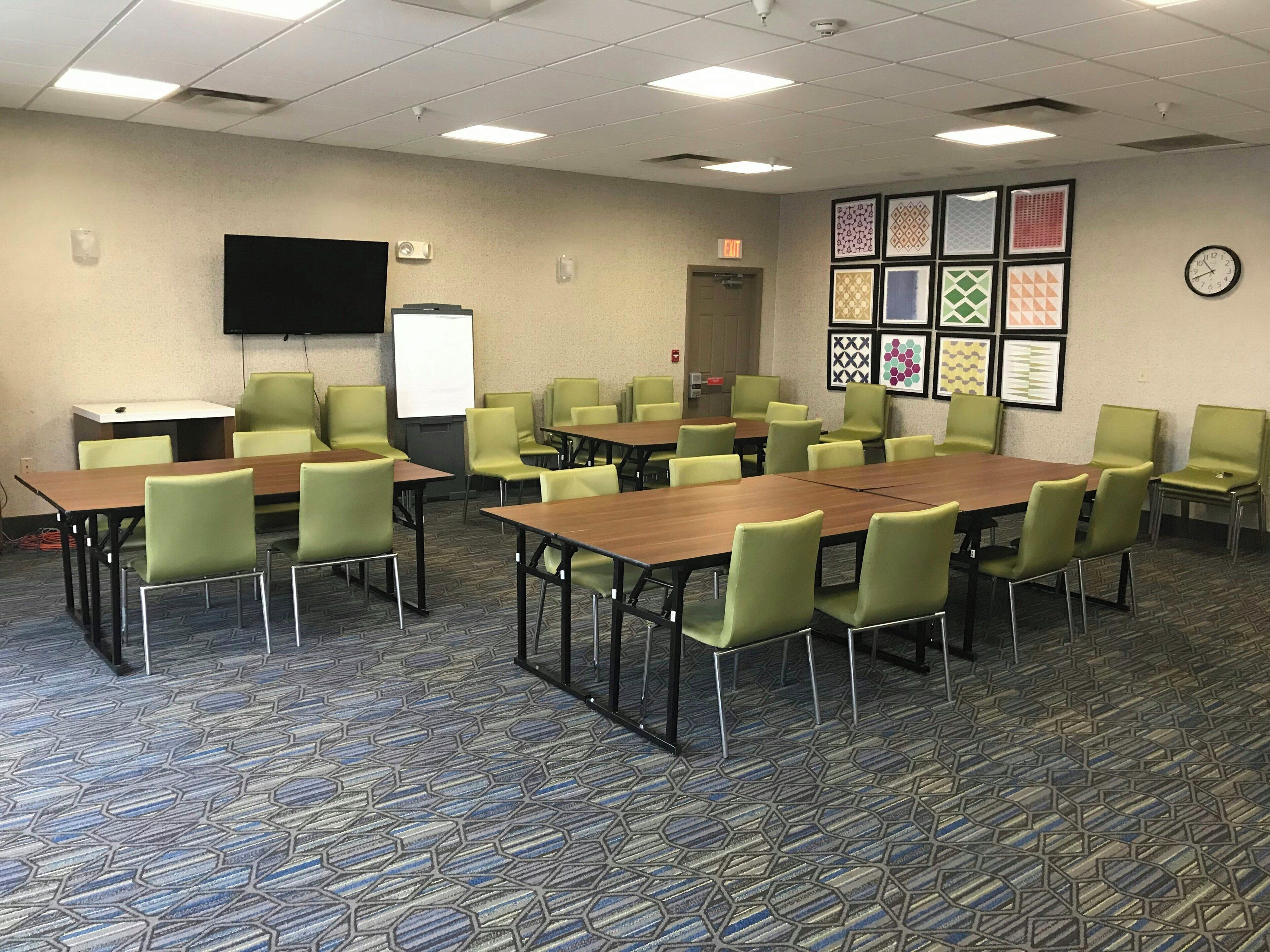 Een vergaderzaal met een grote tafel, meerdere stoelen, een whiteboard, een projectiescherm en decoratieve wandbekleding.