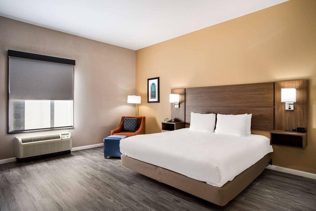 A hotel room with a large bed, a chair, a desk, and a window with blinds.
