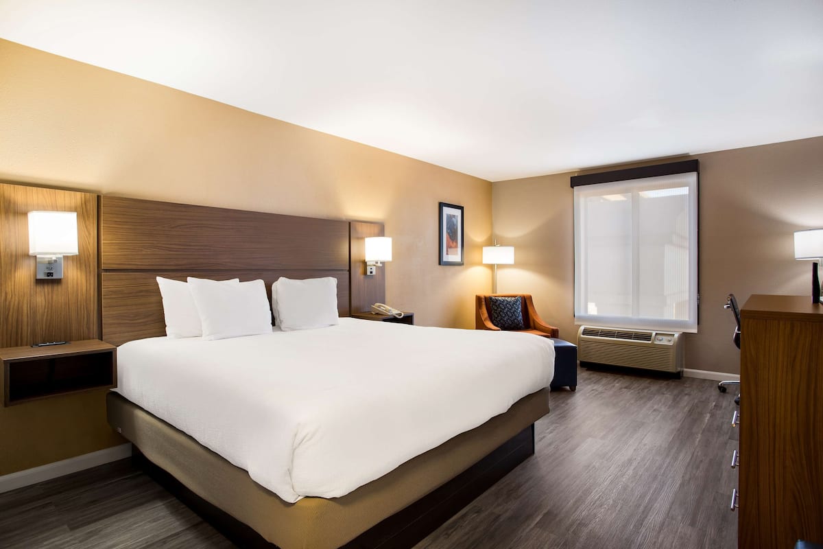 A hotel room with a large bed, bedside tables with lamps, a desk, and a window with blinds.
