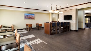 A hotel lobby with wooden tables and chairs, a reception desk, a flat-screen TV, and a painting on the wall.
