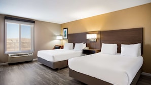A hotel room with two beds, a large window, a wall-mounted heater, and a nightstand with a lamp.