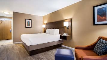 A hotel room with a large bed, a wooden headboard, two bedside lamps, a framed picture on the wall, and a small table with a phone.