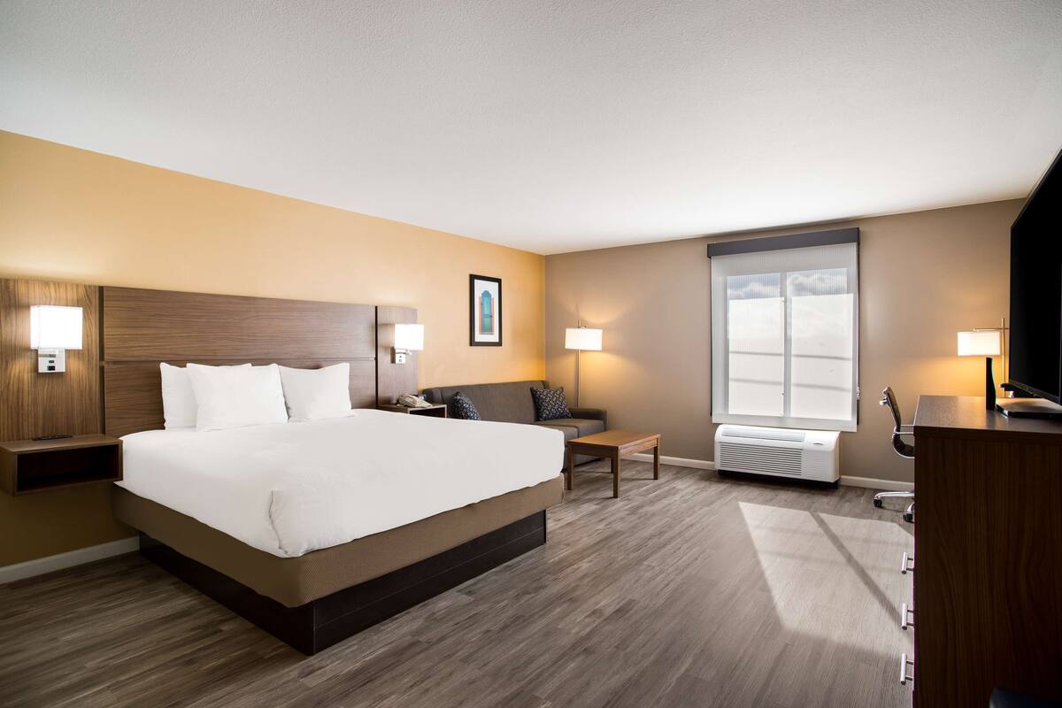 A hotel room with a large bed, a sofa, a desk, and a TV.