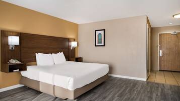 A hotel room with a large bed, wooden headboard, bedside lamps, a framed picture on the wall, and a wooden door.
