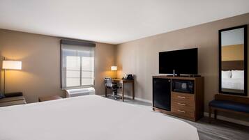 A hotel room with a large bed, a desk with a chair, a television, a microwave, and a bench.