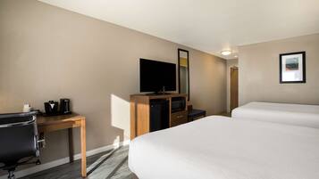 Habitación de hotel con una cama grande, un escritorio con computadora y cafetera, televisión y un cuadro en la pared.