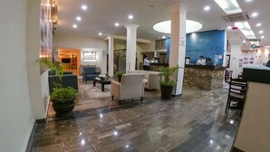 Vestíbulo de hotel con mostrador de recepción, zona de estar y escalera.
