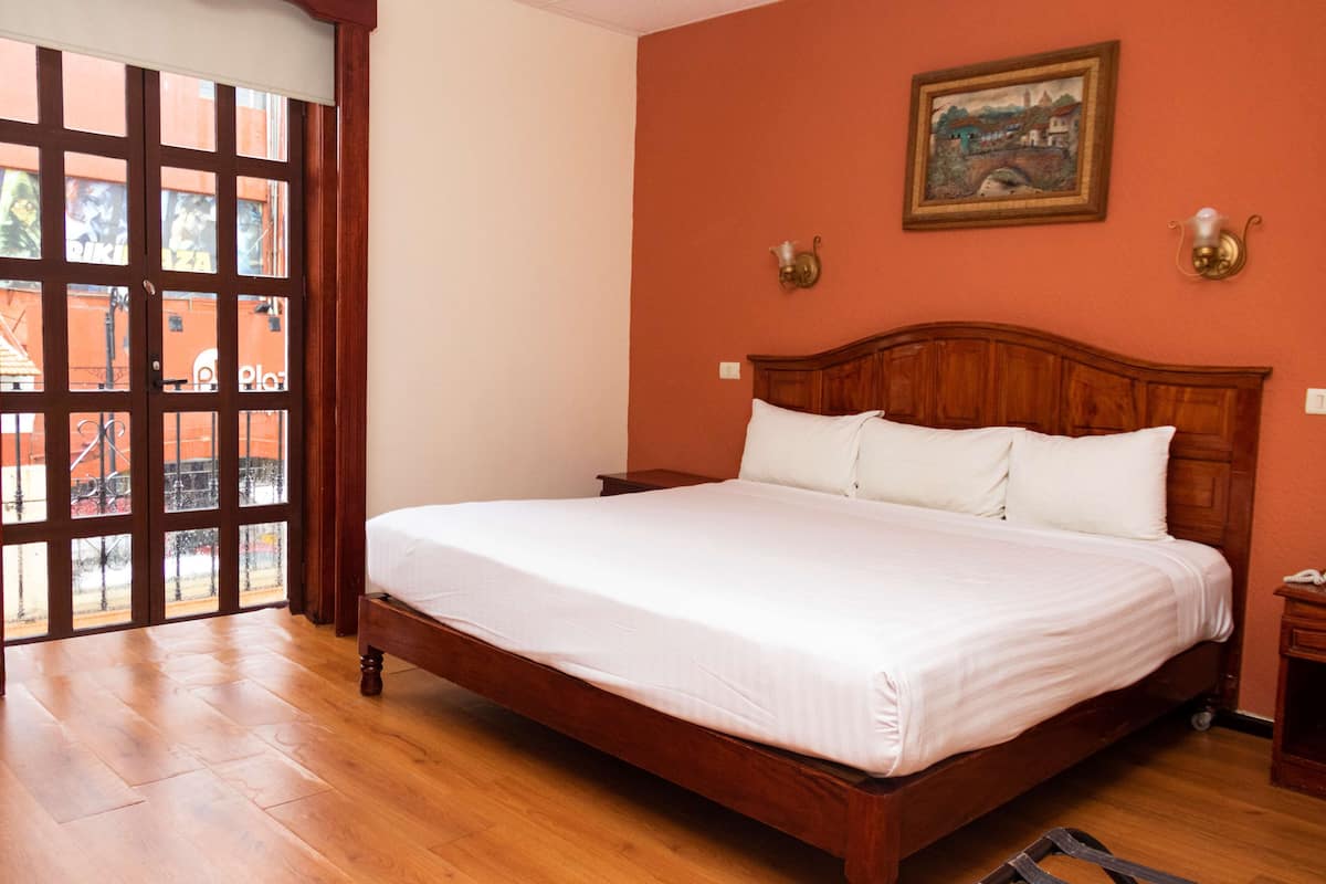 Una cama bien tendida en una habitación con cabecera de madera, un cuadro en la pared y vistas amplias a través de un ventanal.