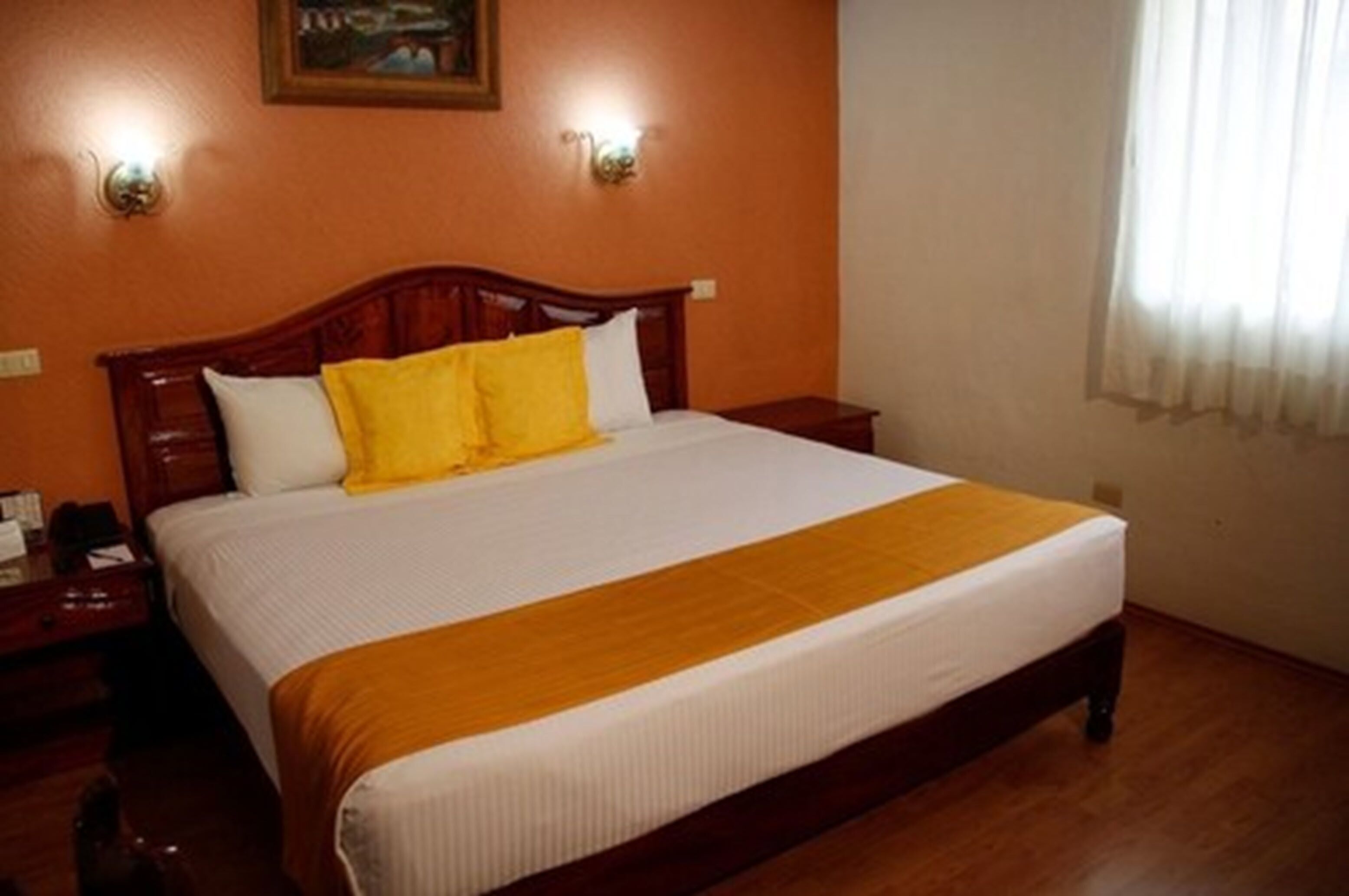 Una cama bien hecha con cabecera de madera, dos mesitas de noche y un cuadro en la pared.