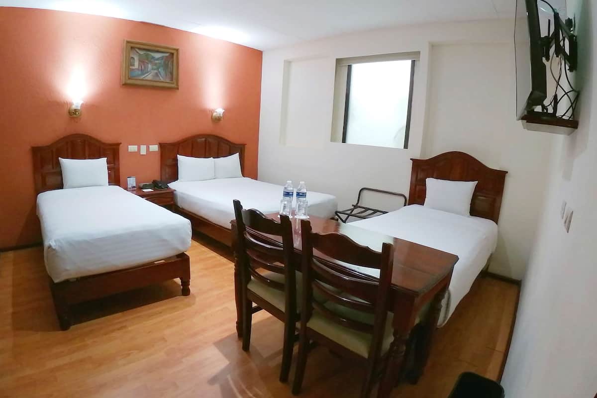Habitación de hotel con dos camas individuales, una mesa de madera con sillas, un escritorio pequeño y una ventana.