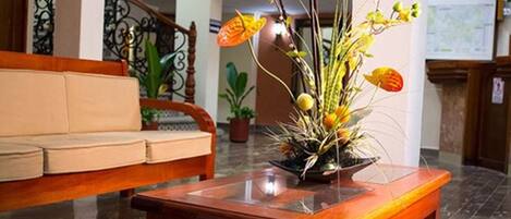 A lobby with a wooden bench, a wooden coffee table with a floral arrangement, and a staircase with a wrought iron railing.