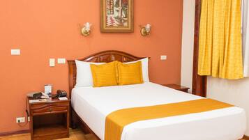 A hotel room with a wooden bed, white bedding, and a yellow throw. There is a nightstand with a phone and a lamp, and a painting on the wall.