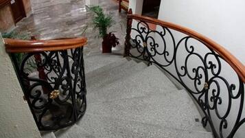 Una escalera con barandilla de hierro forjado negro y pasamanos de madera, que desciende a un nivel inferior.