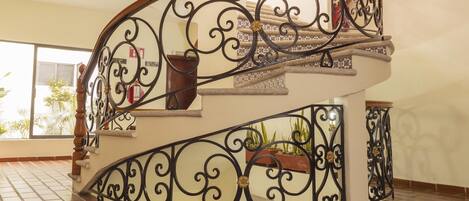 Una escalera curva con barandillas de metal negro decorativas y una pared color crema.