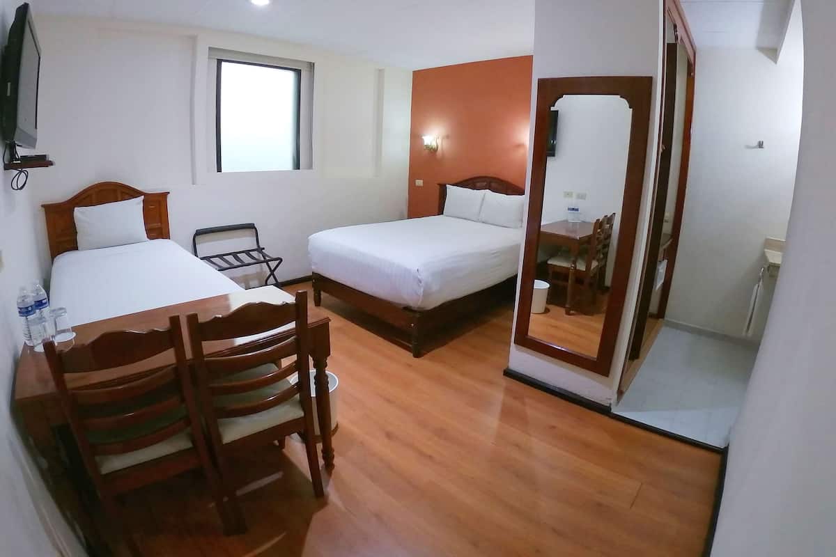 Habitación de hotel con dos camas, una mesa de comedor de madera con sillas, una mesita con una silla, una ventana y un espejo.