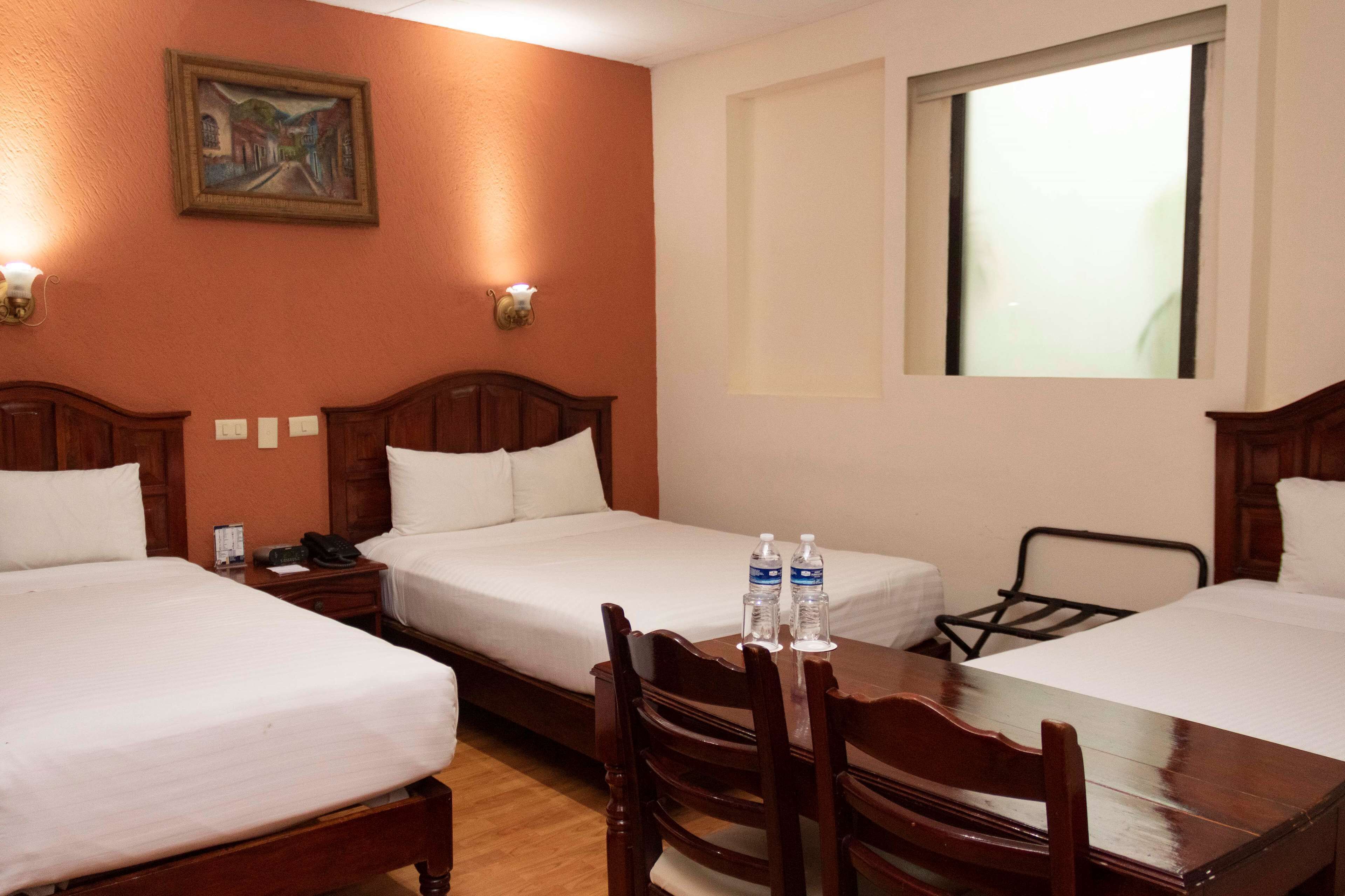 Une chambre d’hôtel avec deux lits simples, une table en bois avec des chaises, un tableau au mur et une fenêtre.