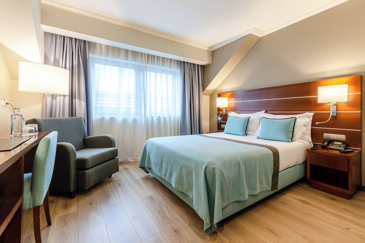 Una habitación de hotel con cama, escritorio, silla, mesita de noche y lámpara.