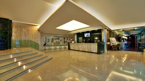 Un vestíbulo amplio con mostrador de recepción, un mural grande y una escalera que lleva a los pisos superiores.