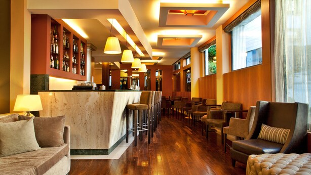 Una zona de bar con mostrador de mármol, varios taburetes y diferentes opciones de asiento, incluyendo sofás y sillones.