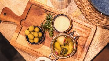 A wooden table with a plate of steak, a bowl of olives, and a jar of pickles.