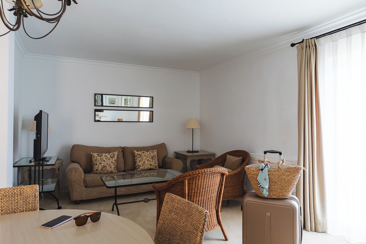 A modern living room with a sofa, coffee table, wicker chairs, a TV, and a lamp.