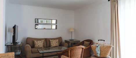 A modern living room with a sofa, coffee table, wicker chairs, a TV, and a lamp.