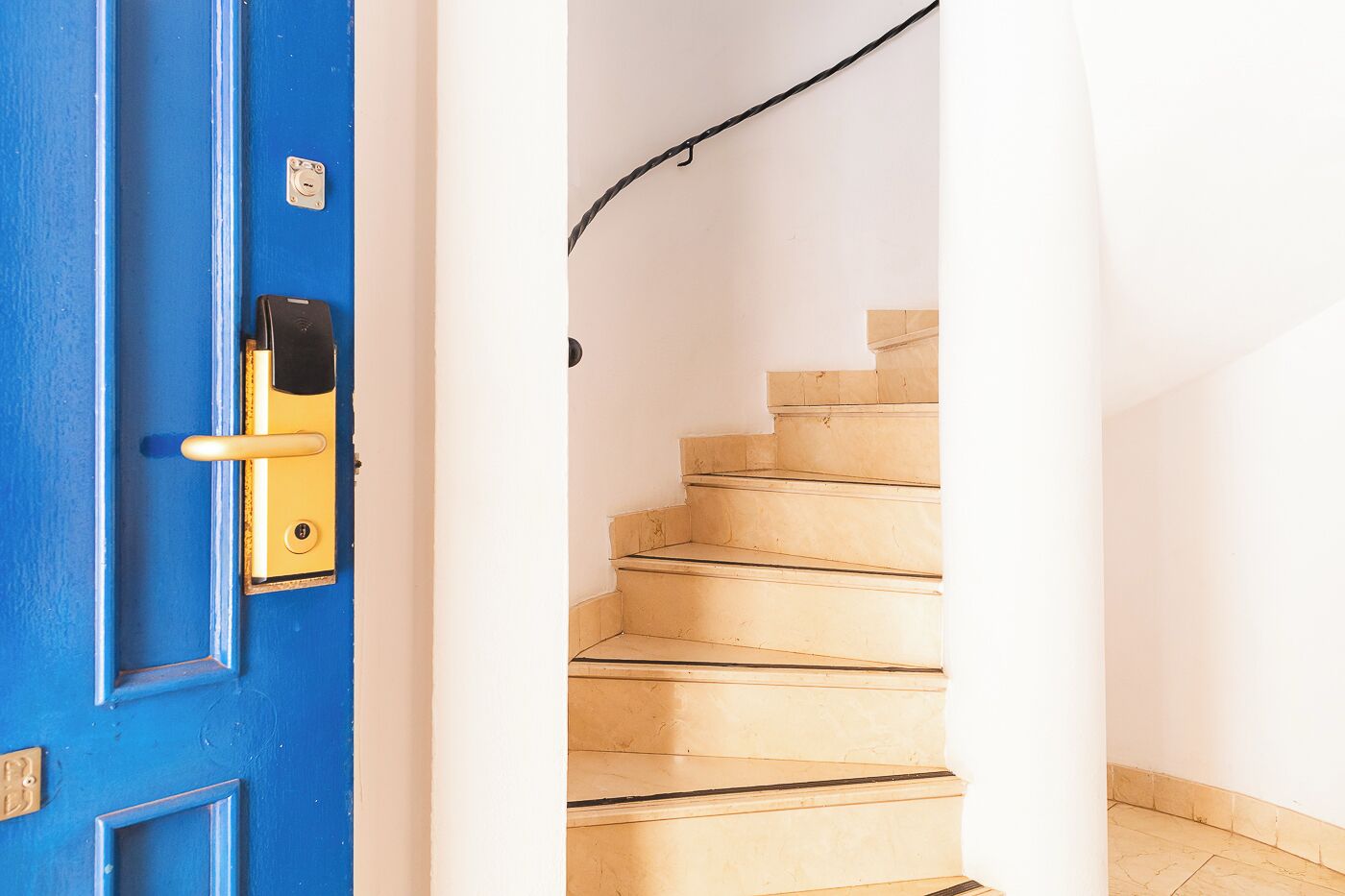 A blue door with a keyhole and a lock, leading to a wooden staircase with white walls.