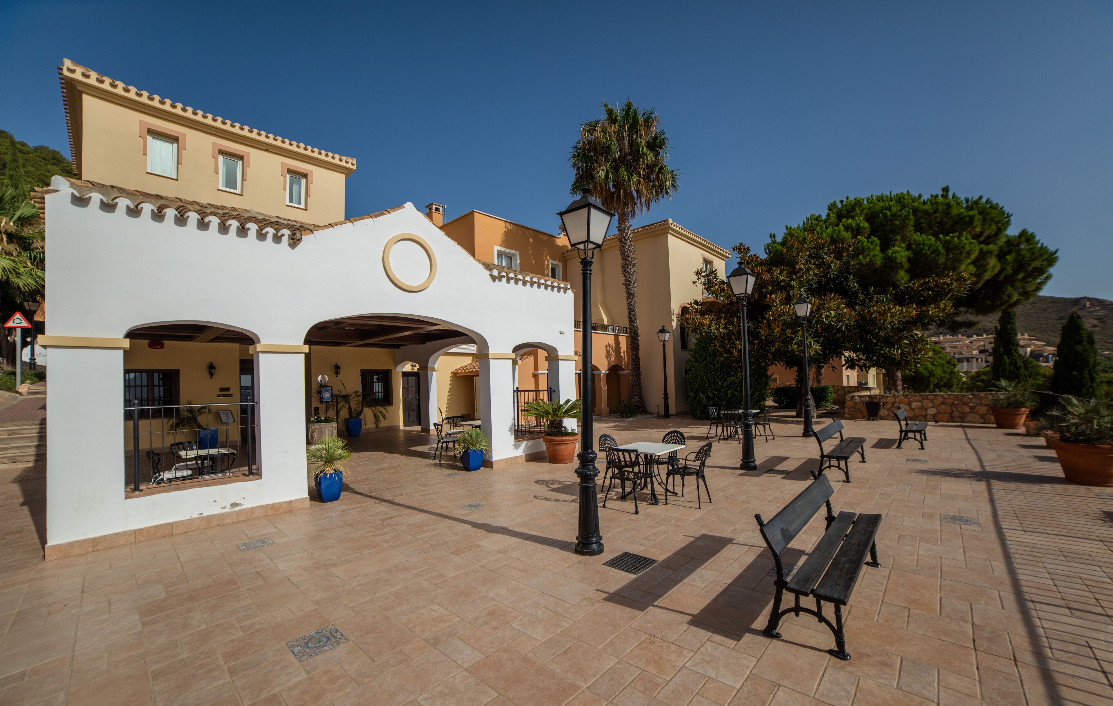 A courtyard with outdoor seating, palm trees, and a building with arches.