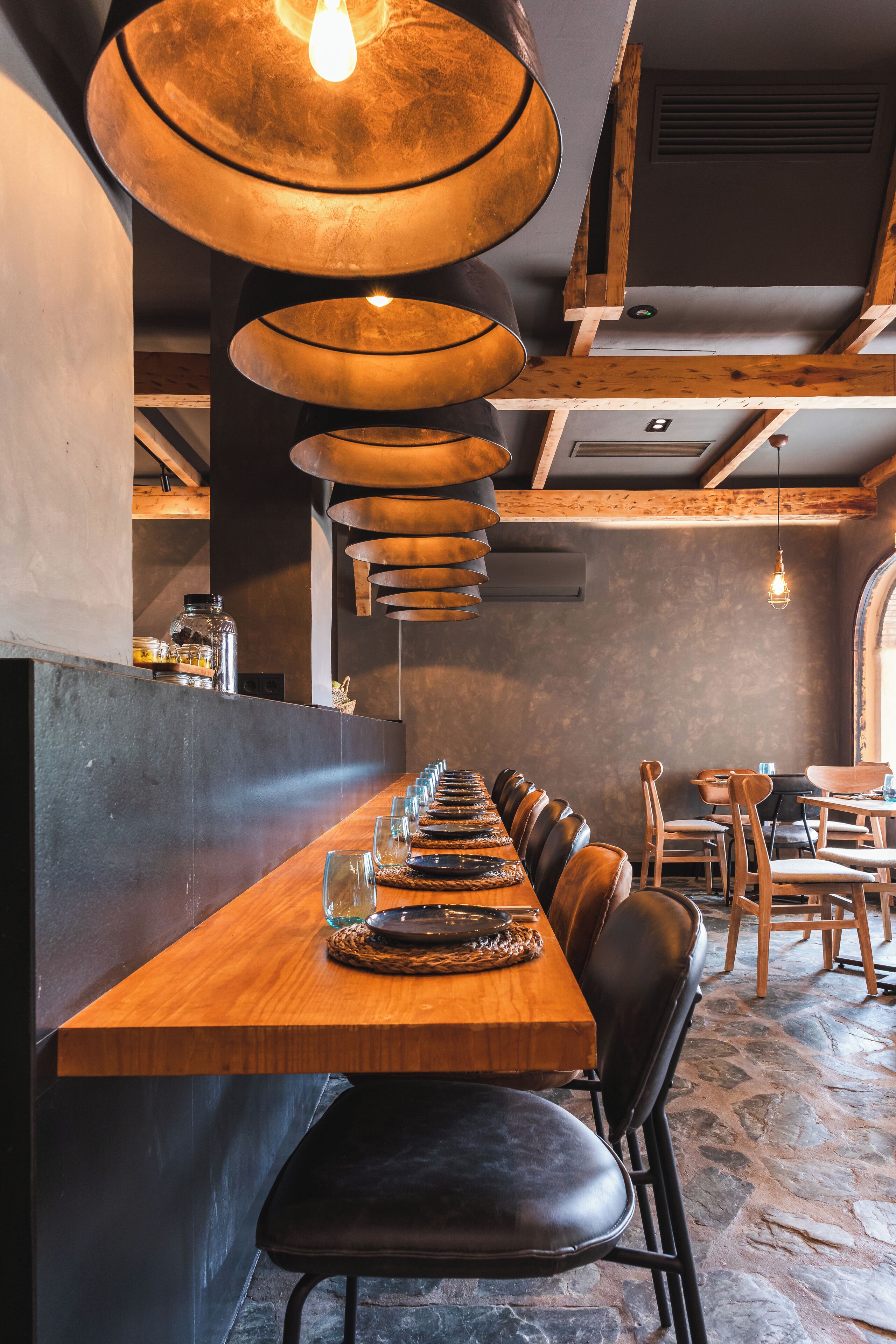 Interior de restaurante con una larga mesa de madera, sillas de cuero negro y una lámpara de techo original.
