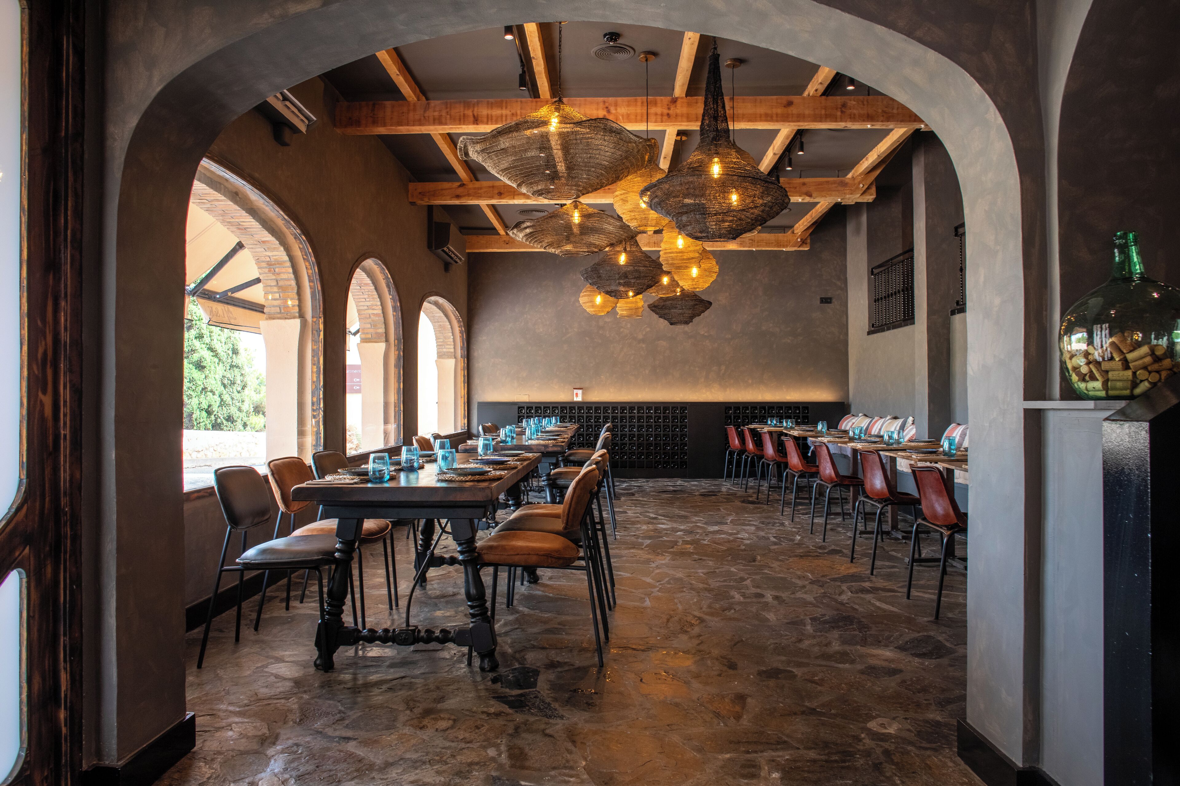 A restaurant with a stone floor, wooden beams, and a long table with chairs.
