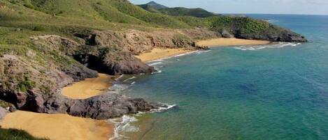 Un paisaje costero con playa de arena, aguas azules cristalinas y colinas verdes.