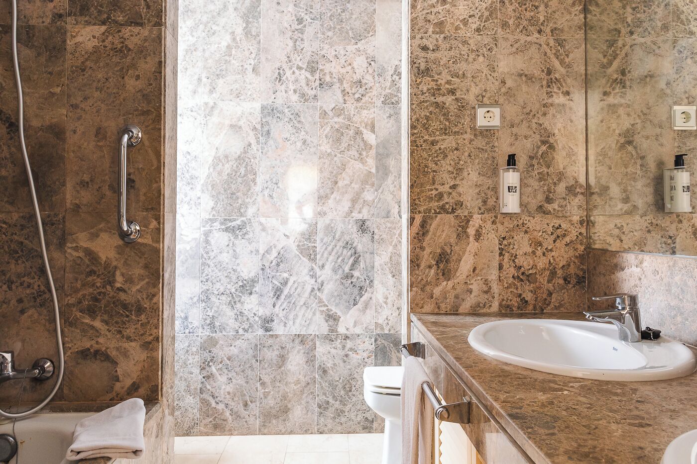 A bathroom with a marble shower, a sink, and a toilet.