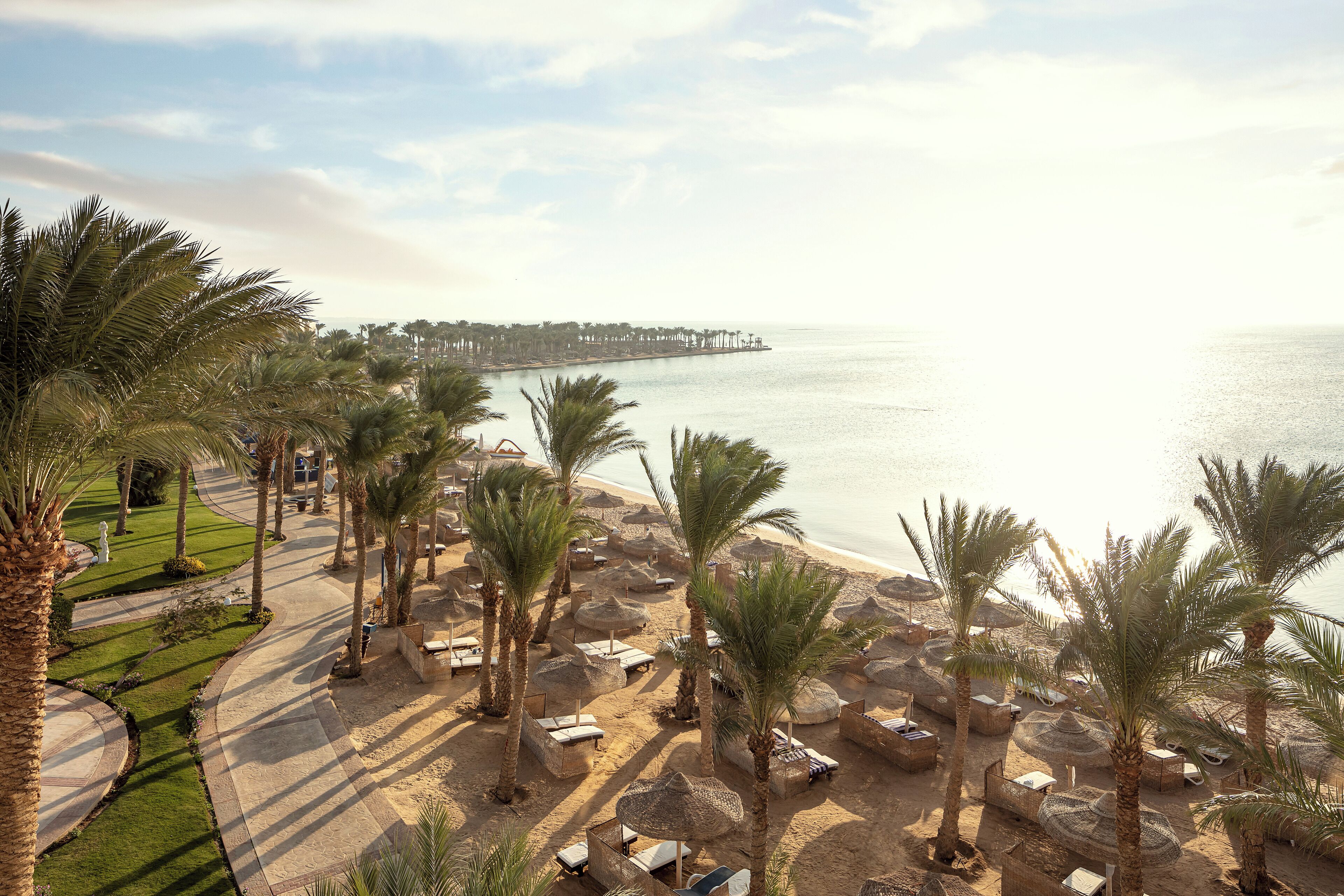 A beach resort with palm trees, sun loungers, and a pier in the background.